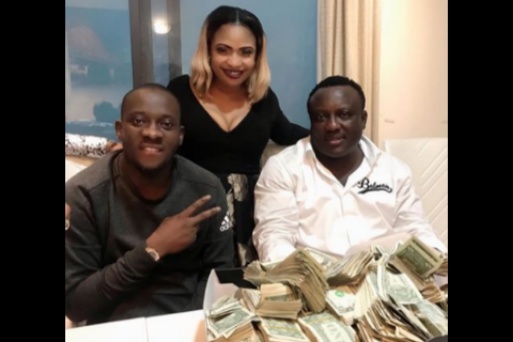 Laide Bakare poses with wads of $1 bills, alongside Saheed Osupa
